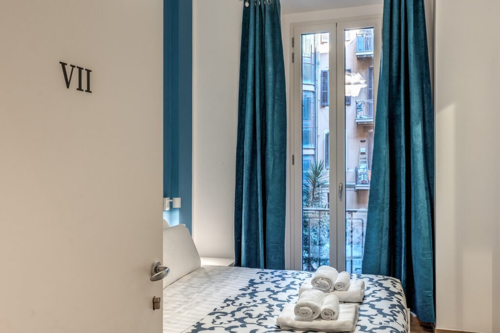 Camera con letto matrimoniale, tende blu e finestra – Orazio B&B Roma
